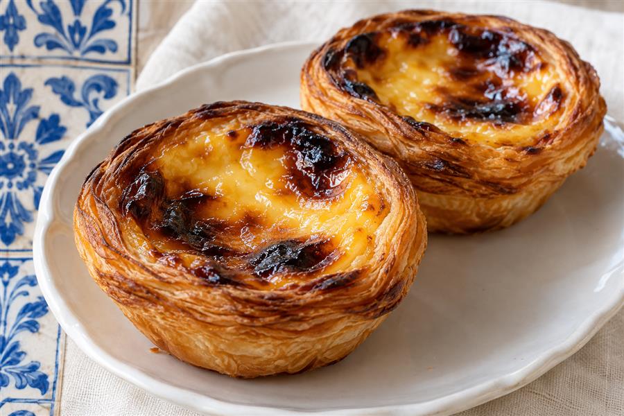 Golden Portuguese custard tarts on a white plate beside blue azulejo tiles